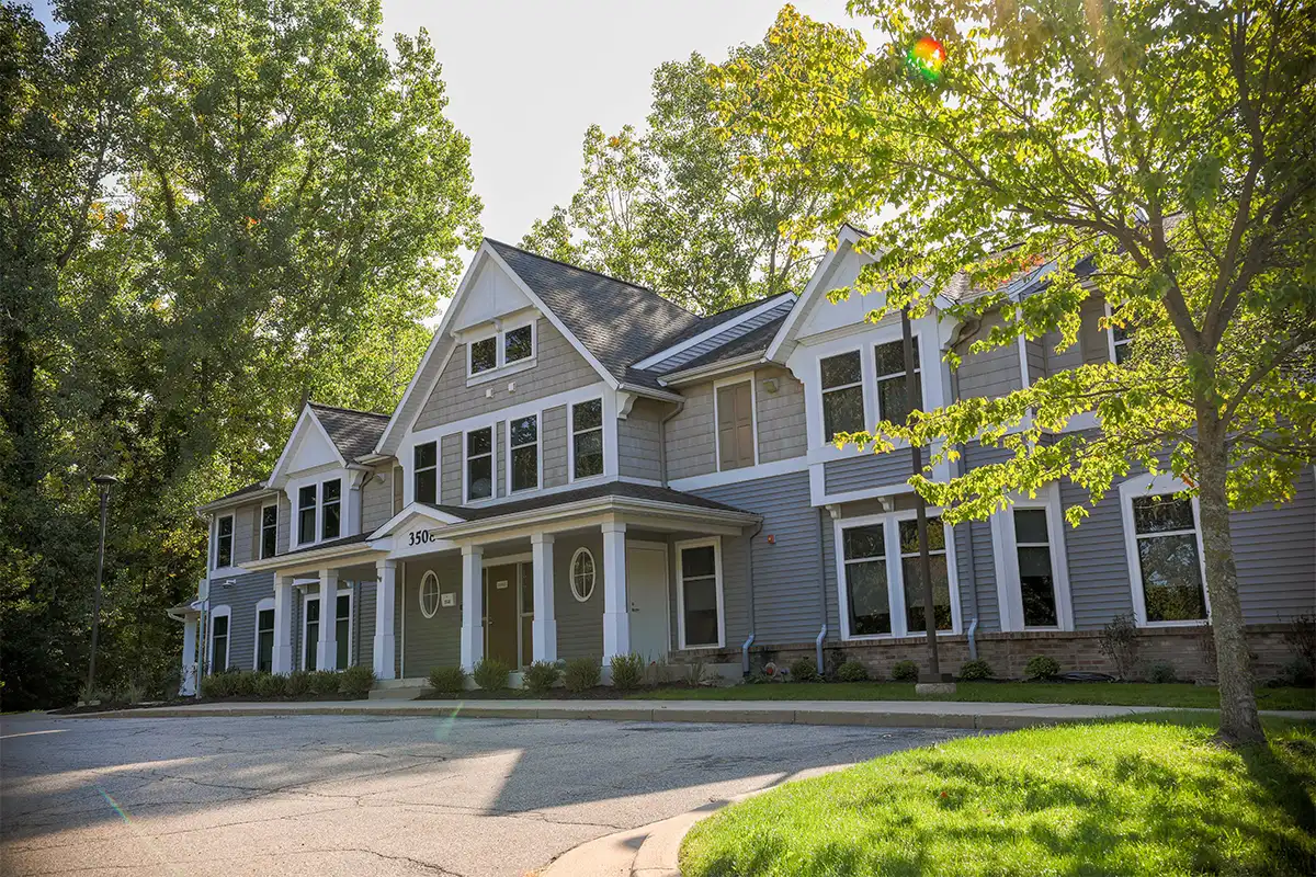 Two-story gray building with white porch columns and a 350c address sign, surrounded by trees
