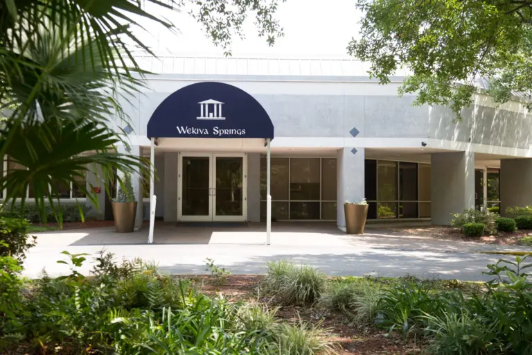 Entrance of a gray one-story building with a navy Wekiva Springs awning and landscaped walkway