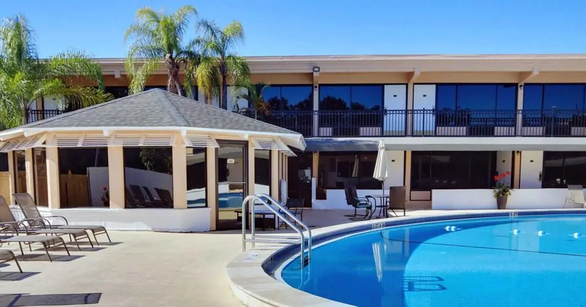 Two-story beige building with a pool and gazebo-style structure under palm trees