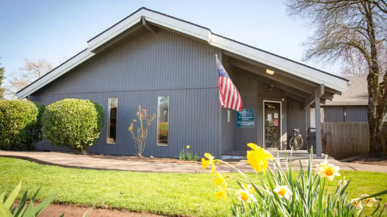 Gray single-story building with a Willamette Family Men's Residential Services sign and an American flag