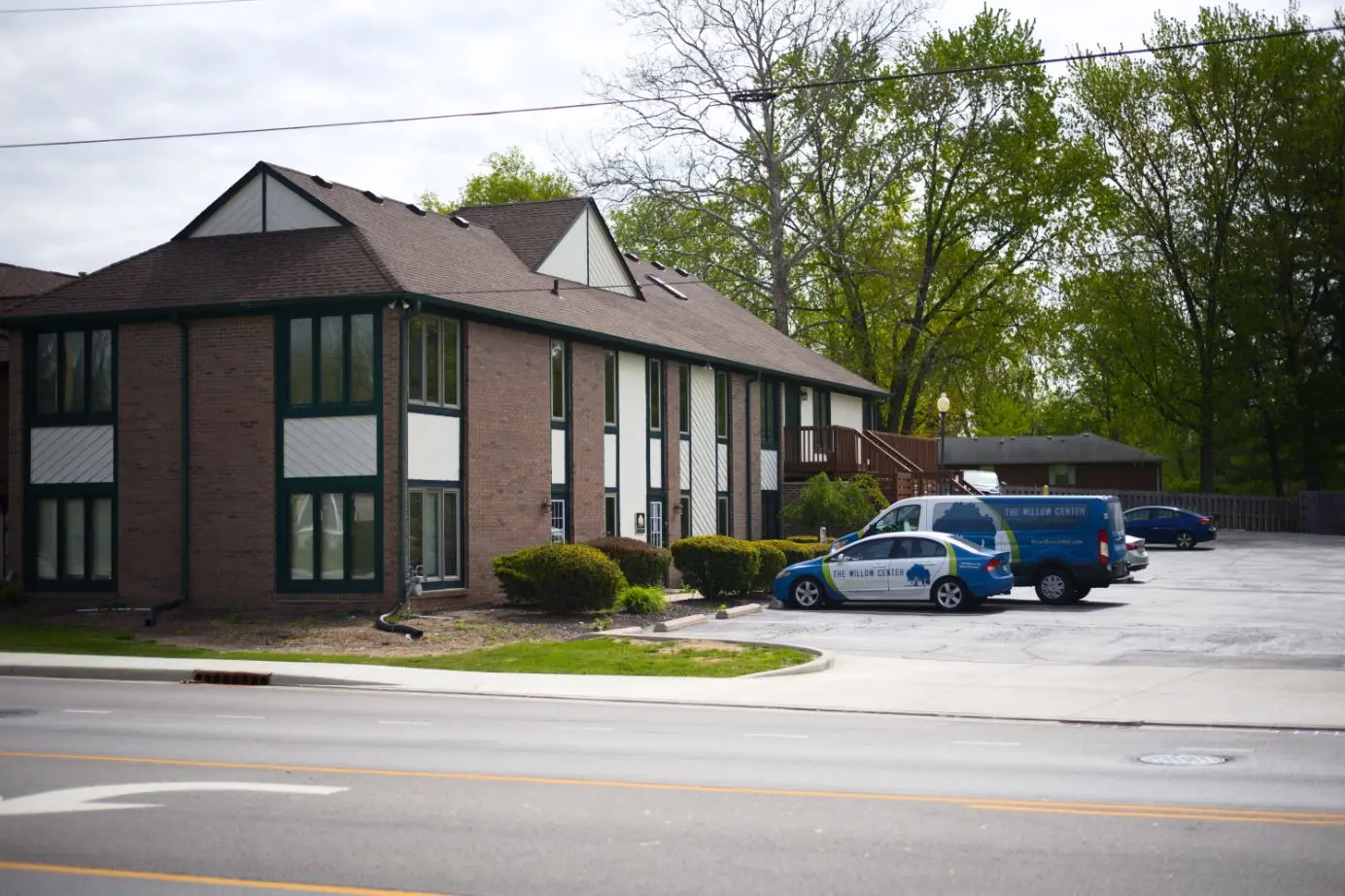 Two-story brick building with green trim and Willow Center vehicles parked in the lot