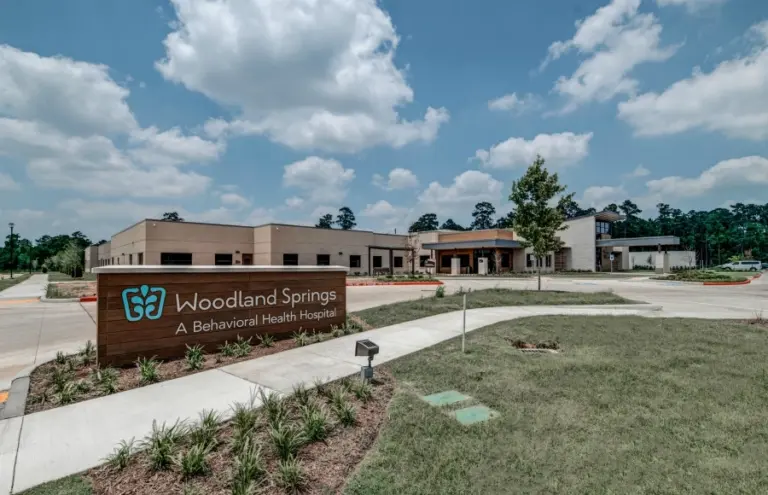 Single-story building with a wood monument sign reading Woodland Springs, A Behavioral Health Hospital