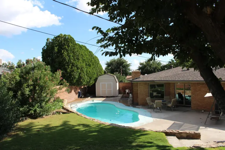Backyard with a pool, patio and brick single-story house under a large tree